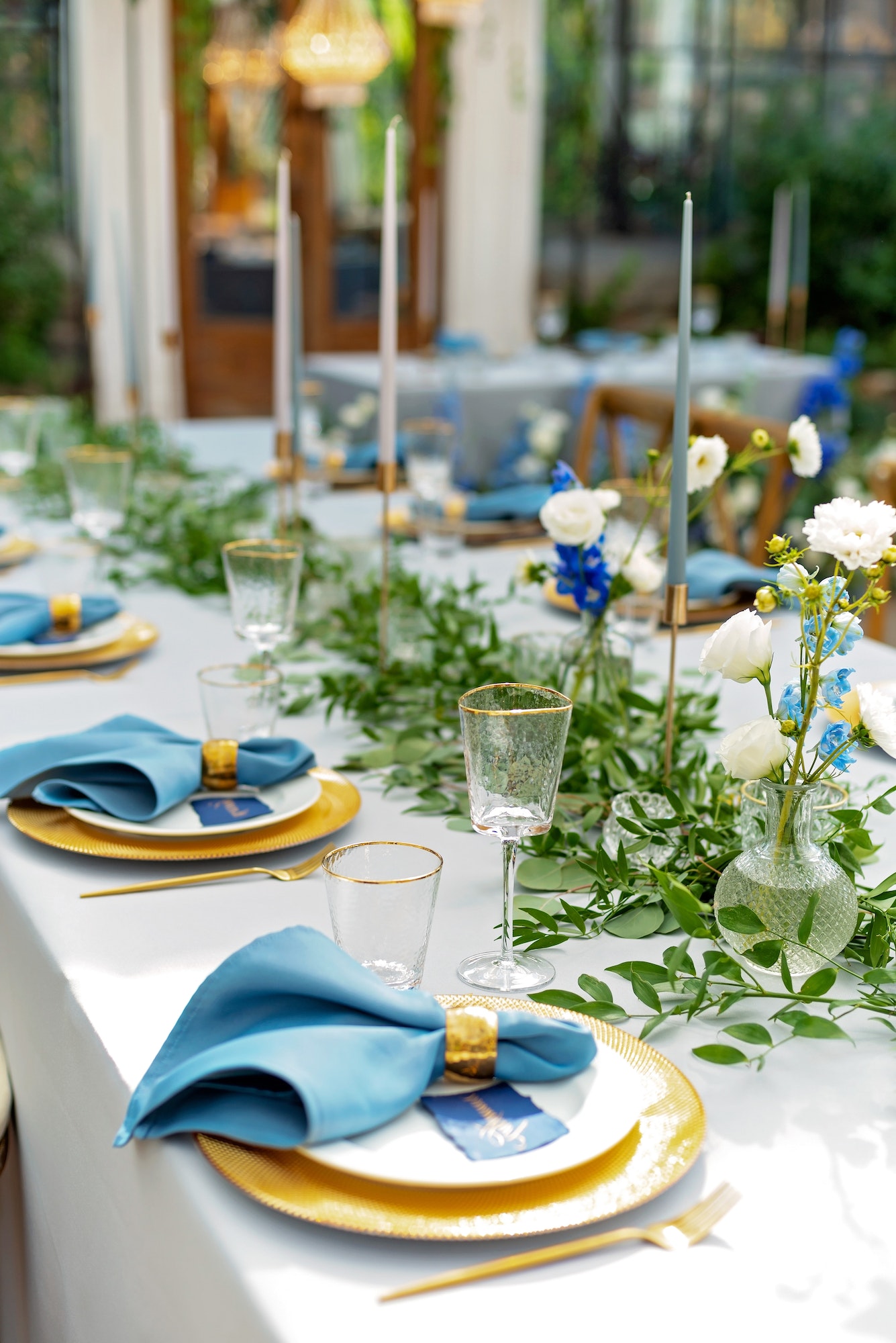 Banquet wedding table setting with blue napkins, gold cutlery, crystal, fresh flowers and candles.